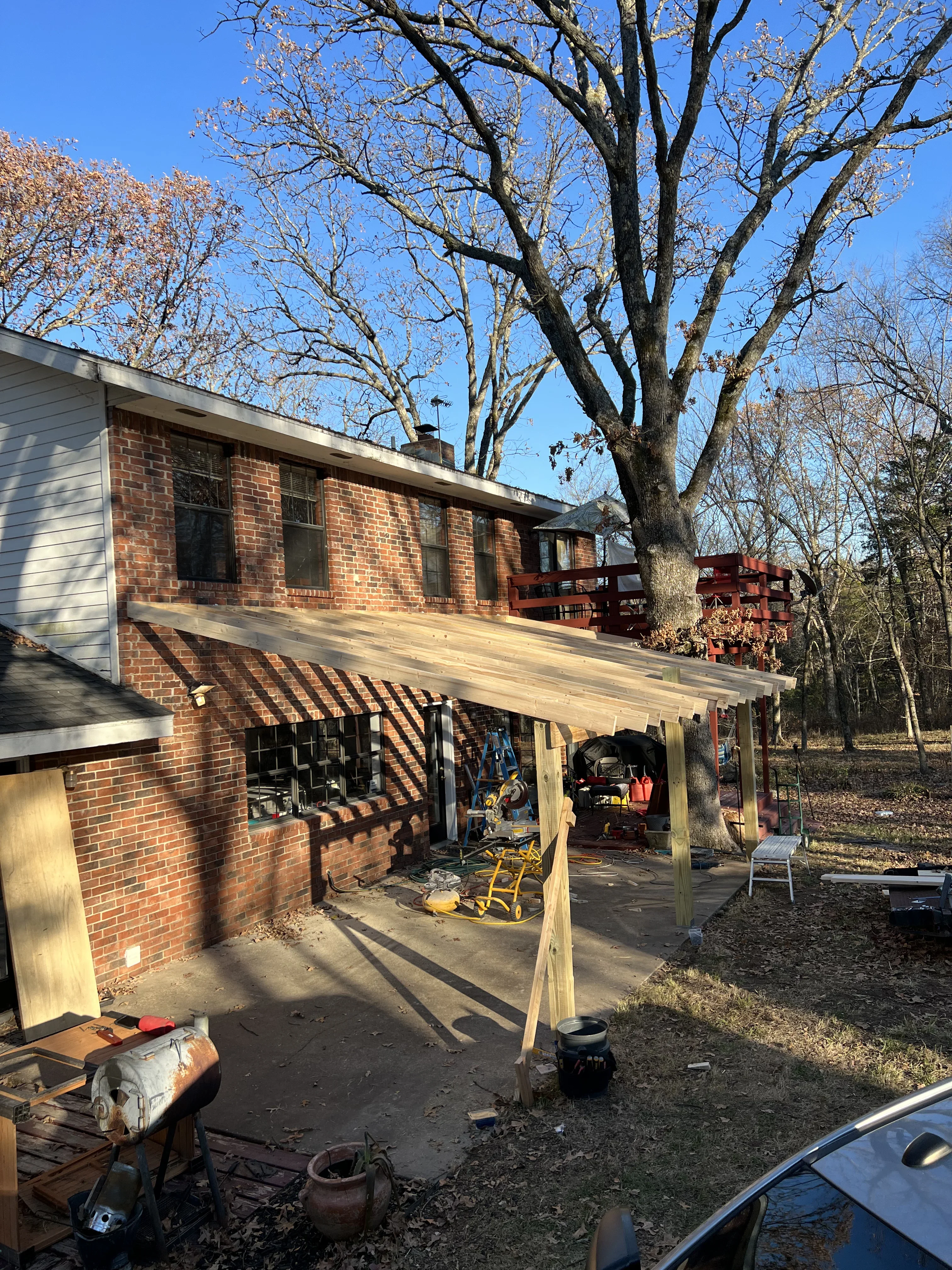 Wood-framed covered patio with posts and beams attached to brick house