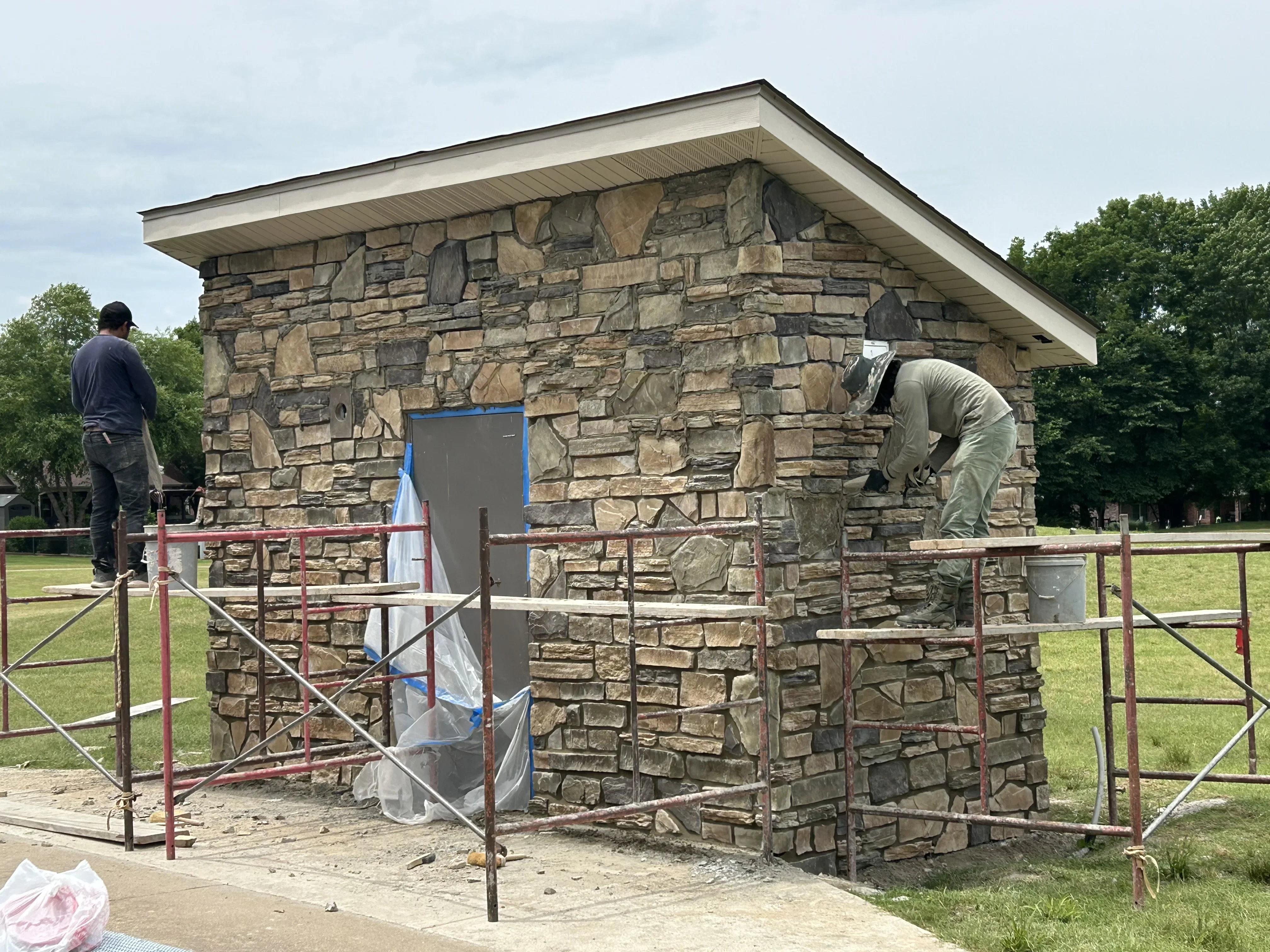 Stone masonry utility building with stacked natural stone walls and metal roof under construction