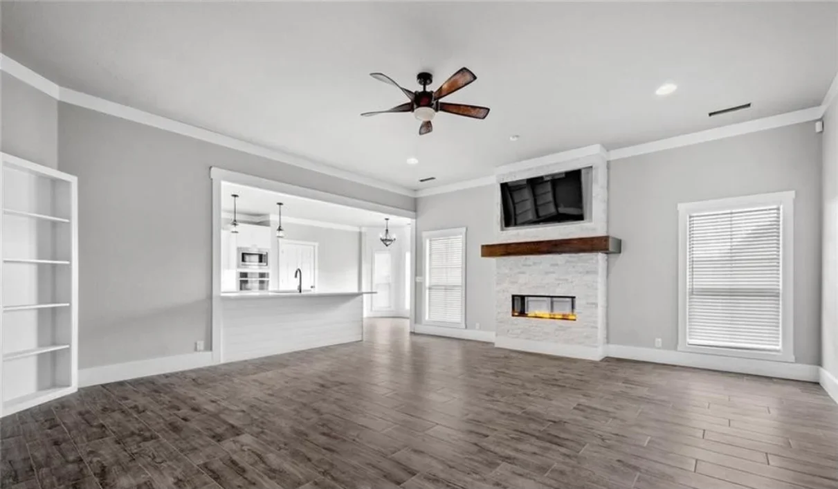 Open living room with hardwood floors, fireplace with marble surround, wood mantel, and modern kitchen