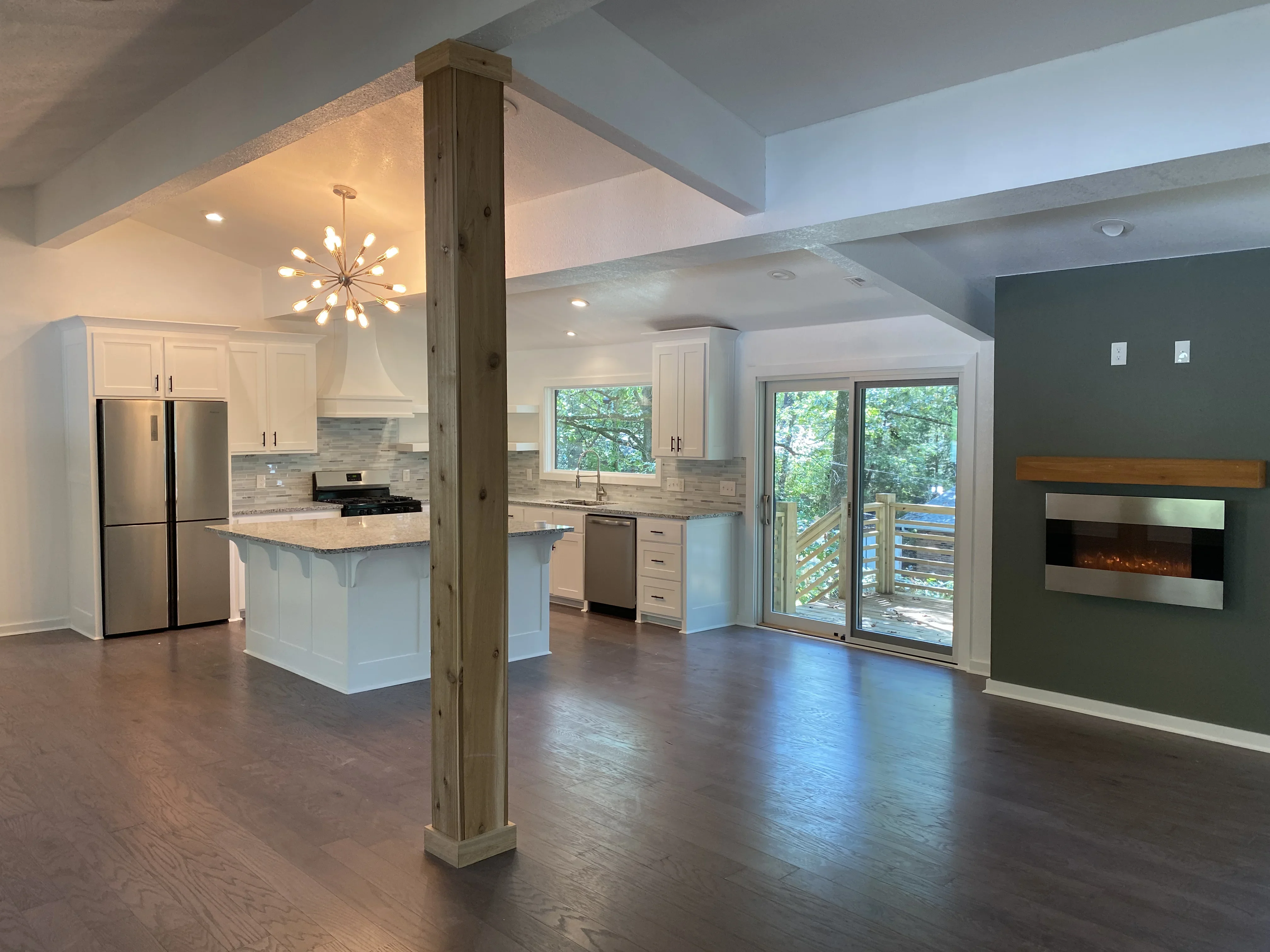 Open kitchen with white cabinets, granite island, hardwood floors, and fireplace accent wall