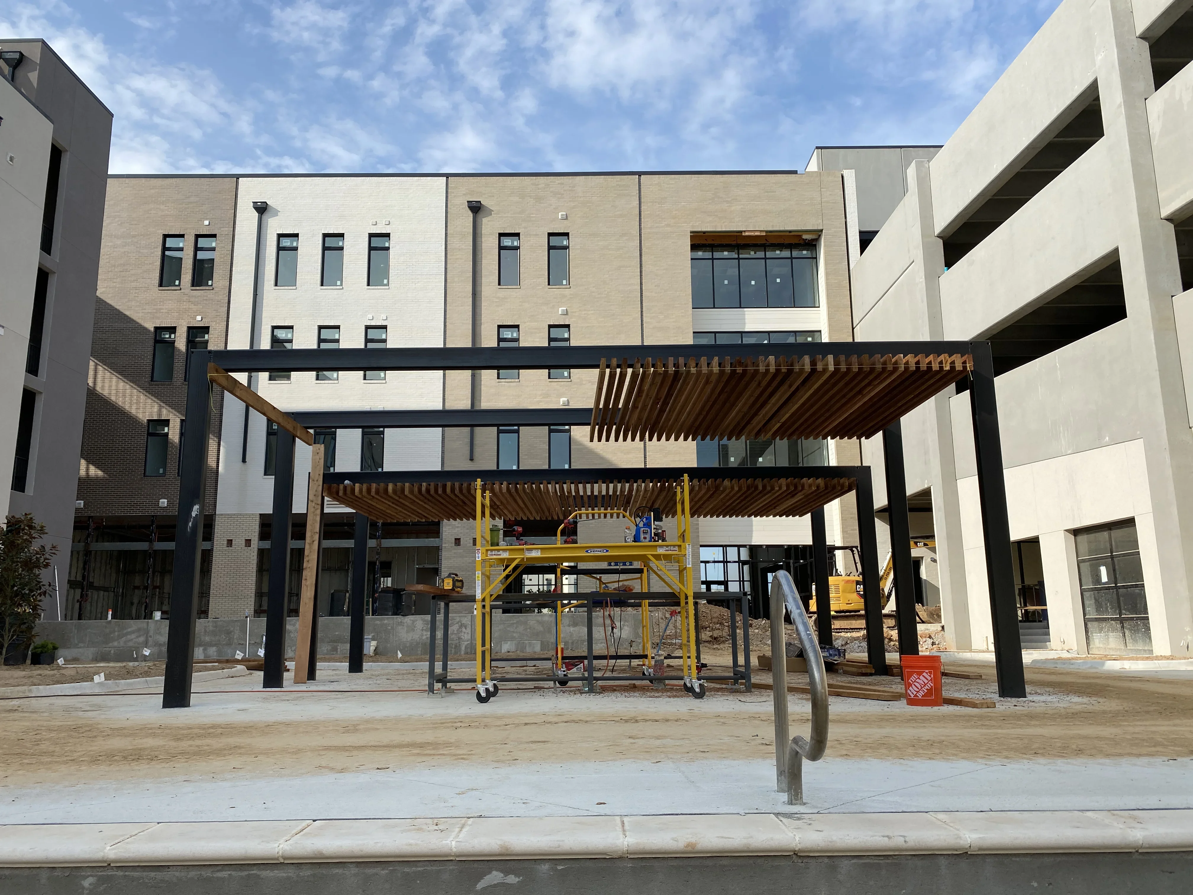 Steel pergola with wood slats and black columns in courtyard of multi-story brick and concrete building under construction