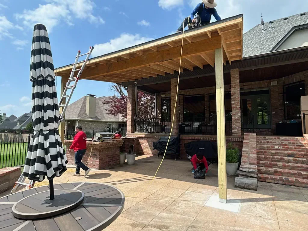 Covered patio with exposed wood beams, concrete pad, and brick home integration during construction