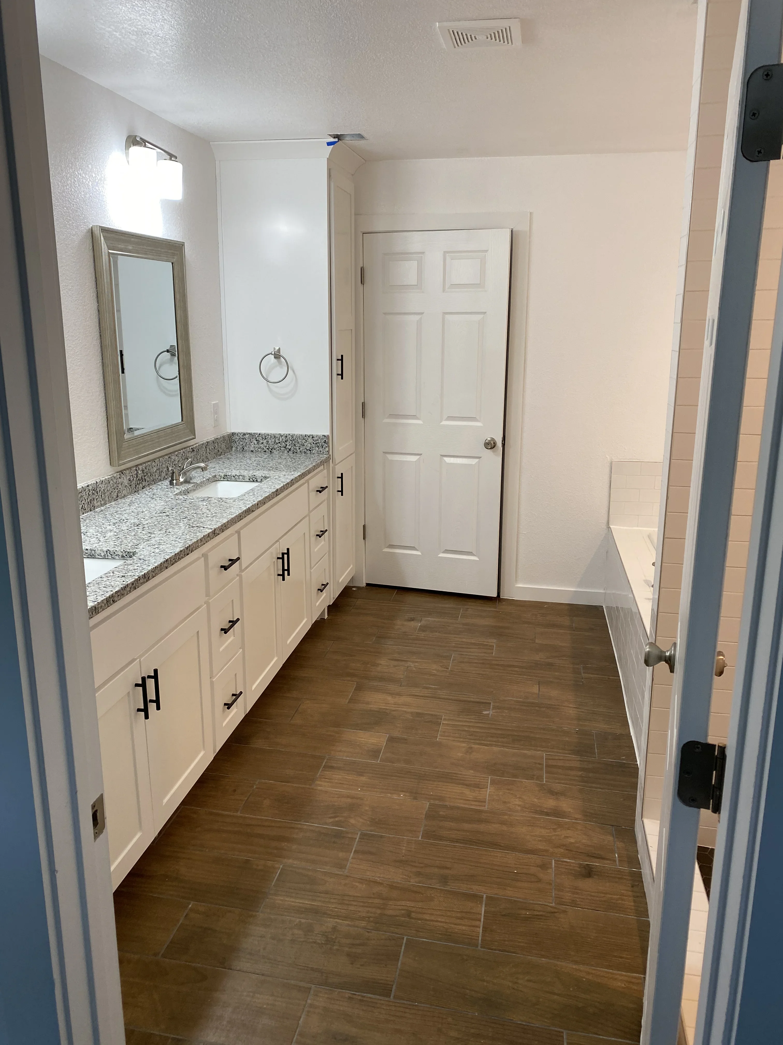 Bathroom vanity with granite countertop, cream cabinets, wood plank flooring, and white tile walls