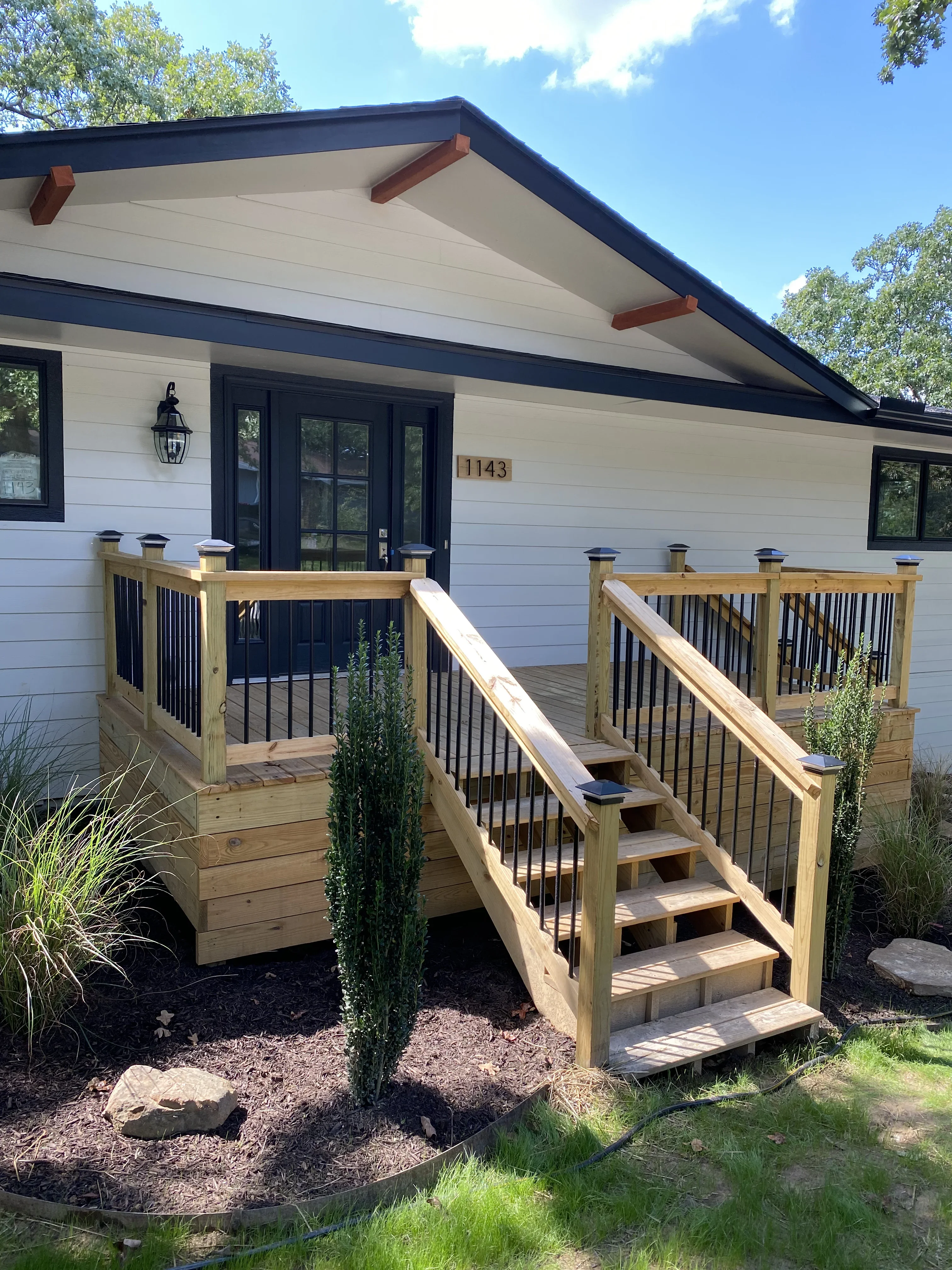 Two-level wood deck with black metal railings, stairs, and natural wood posts attached to modern home