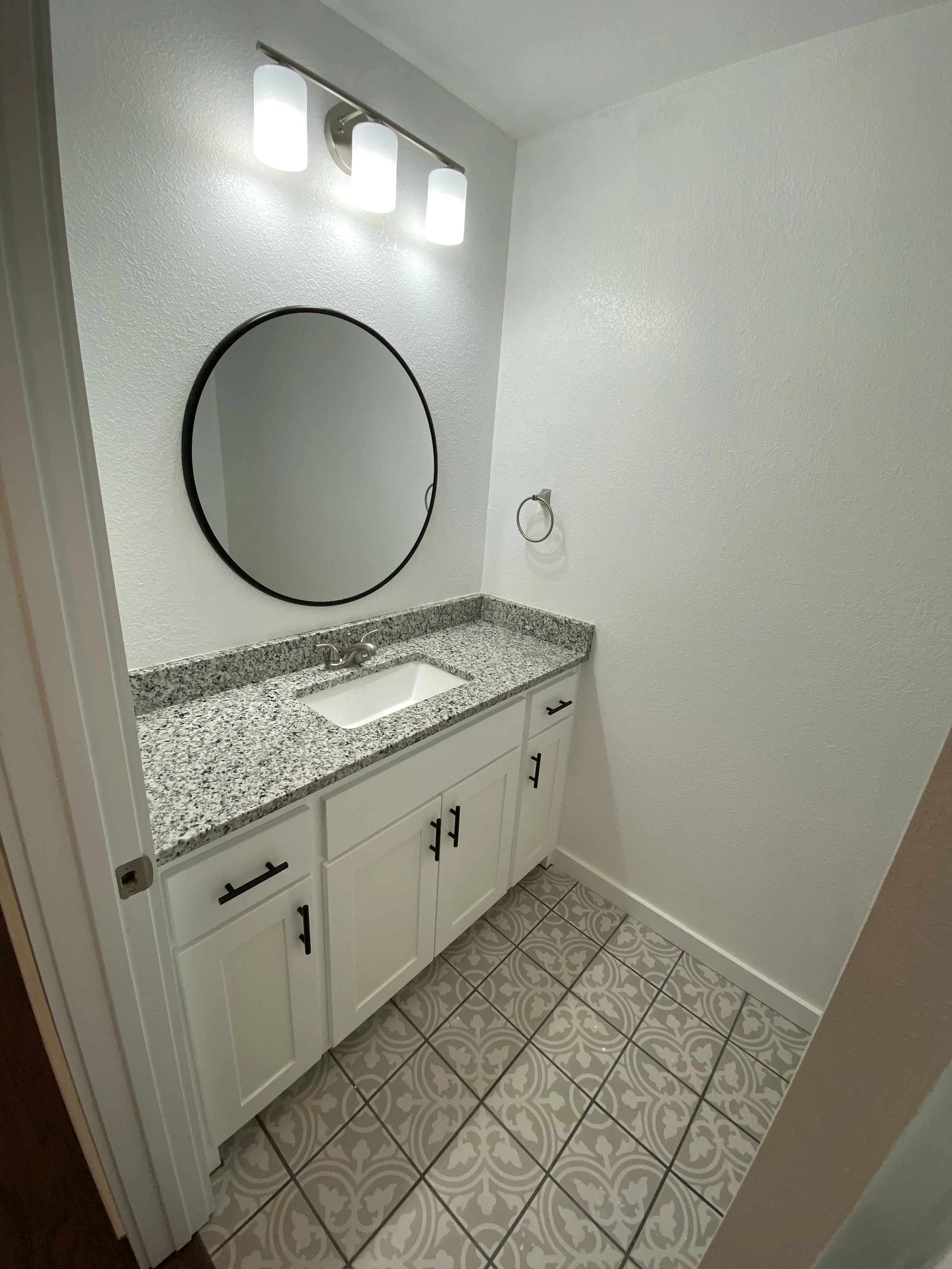 White bathroom vanity with gray quartz countertop, black-framed mirror, and three-light vanity fixture