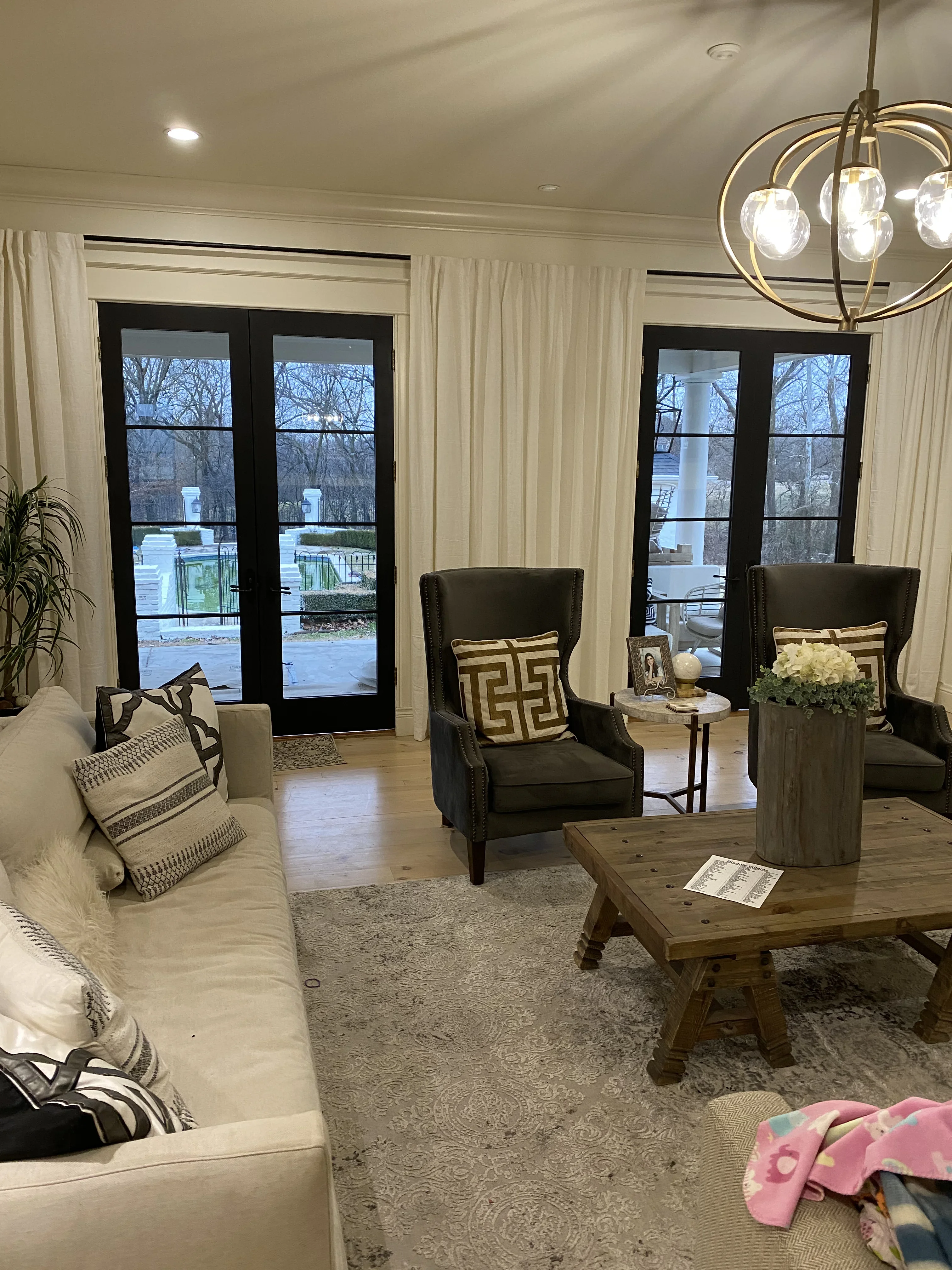 Living room with black French doors, hardwood floors, recessed lights, and brass pendant fixture