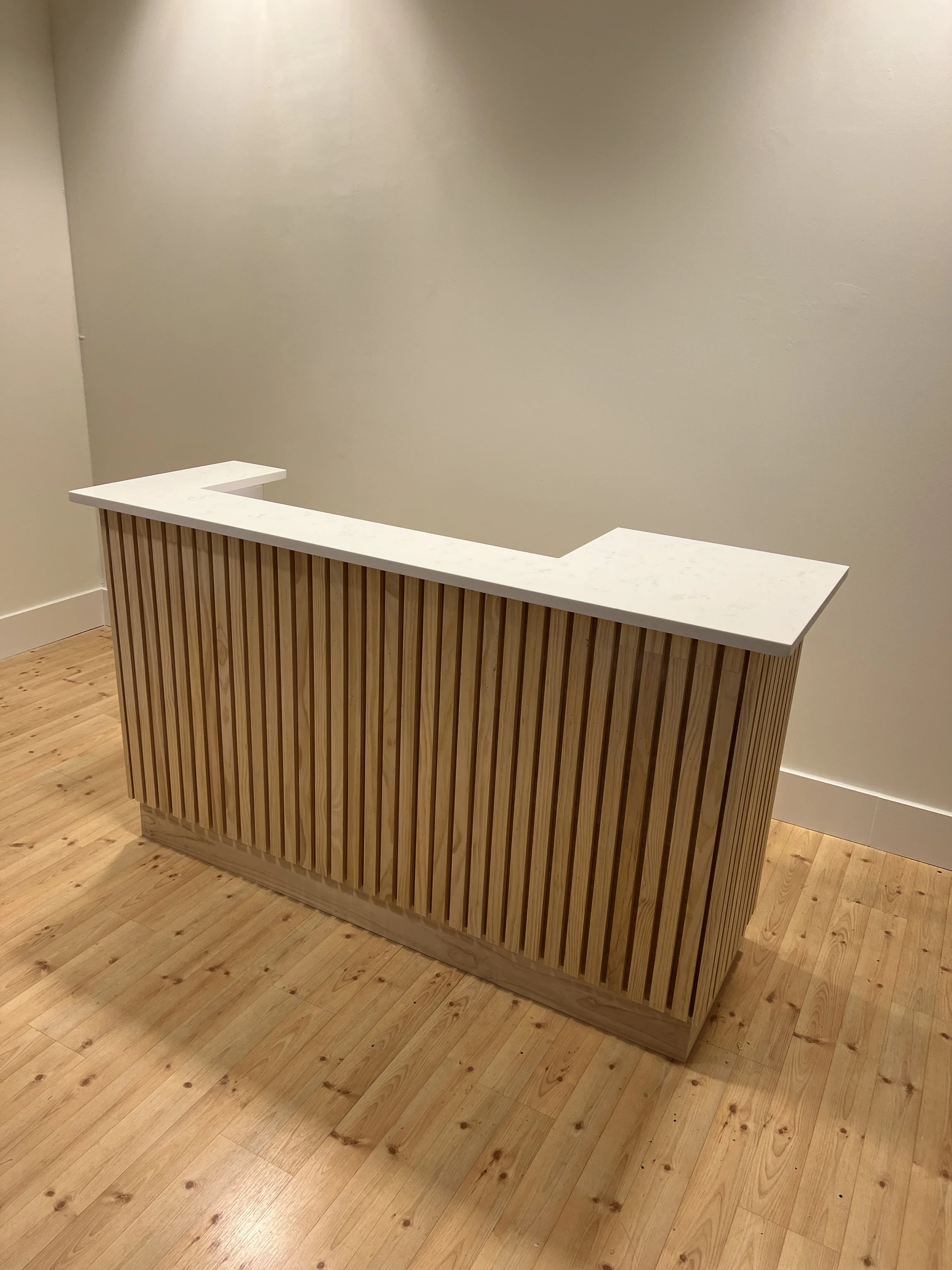 L-shaped reception counter with vertical wood slat paneling and white quartz top