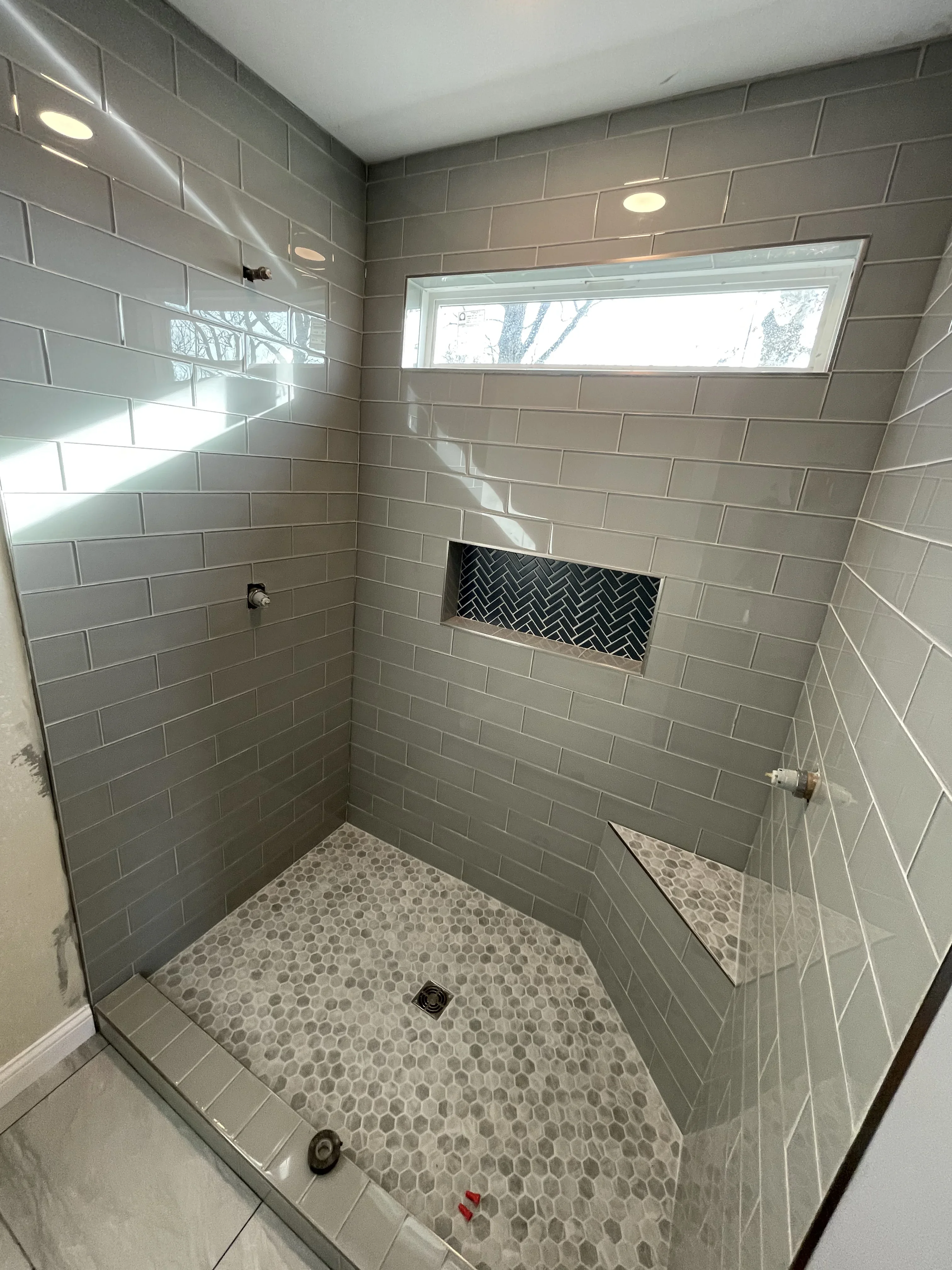Gray subway tile shower with herringbone accent niche, hexagonal floor tile, and frameless glass door