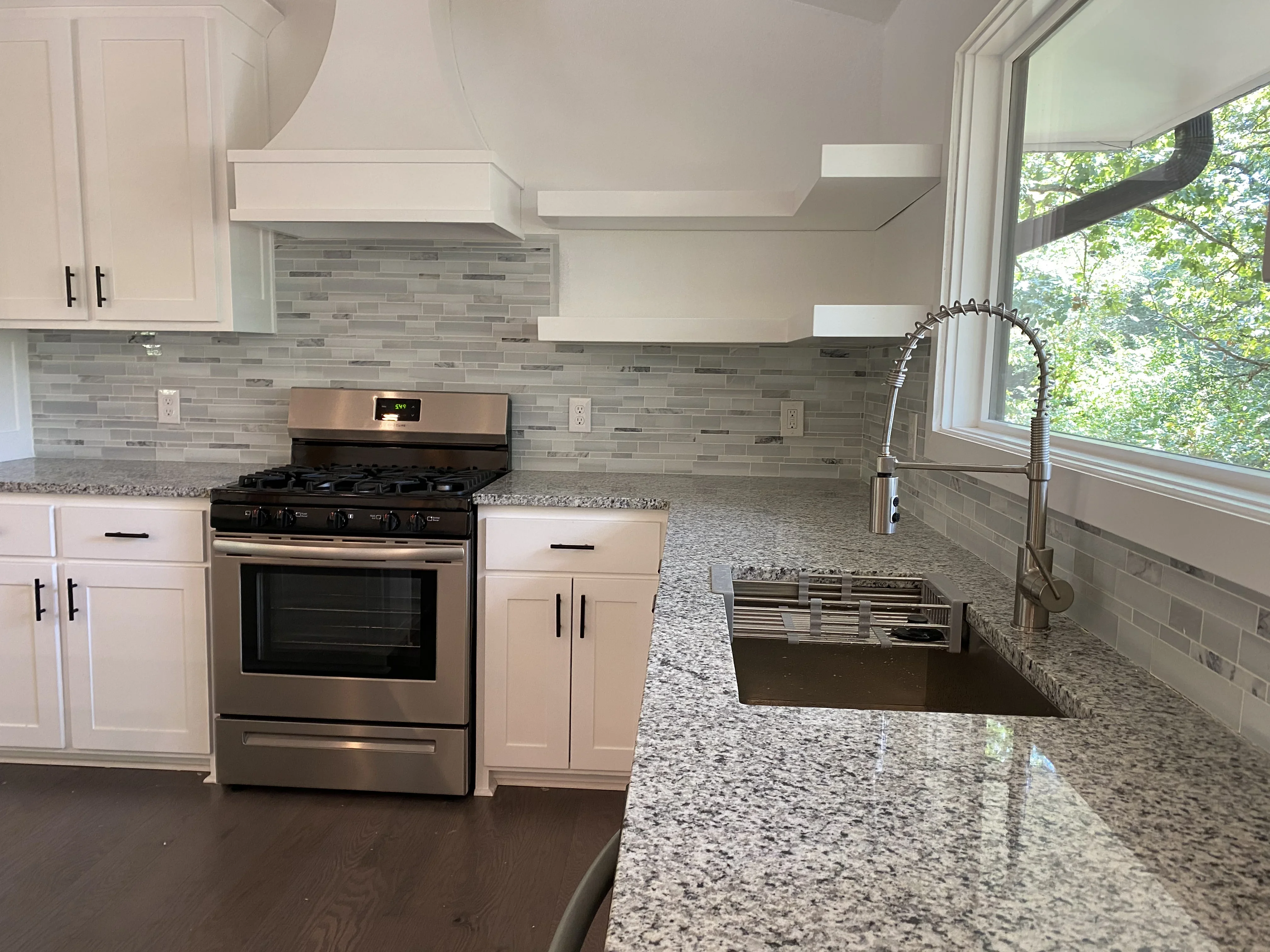 White kitchen cabinets, gray tile backsplash, granite counters, stainless steel appliances