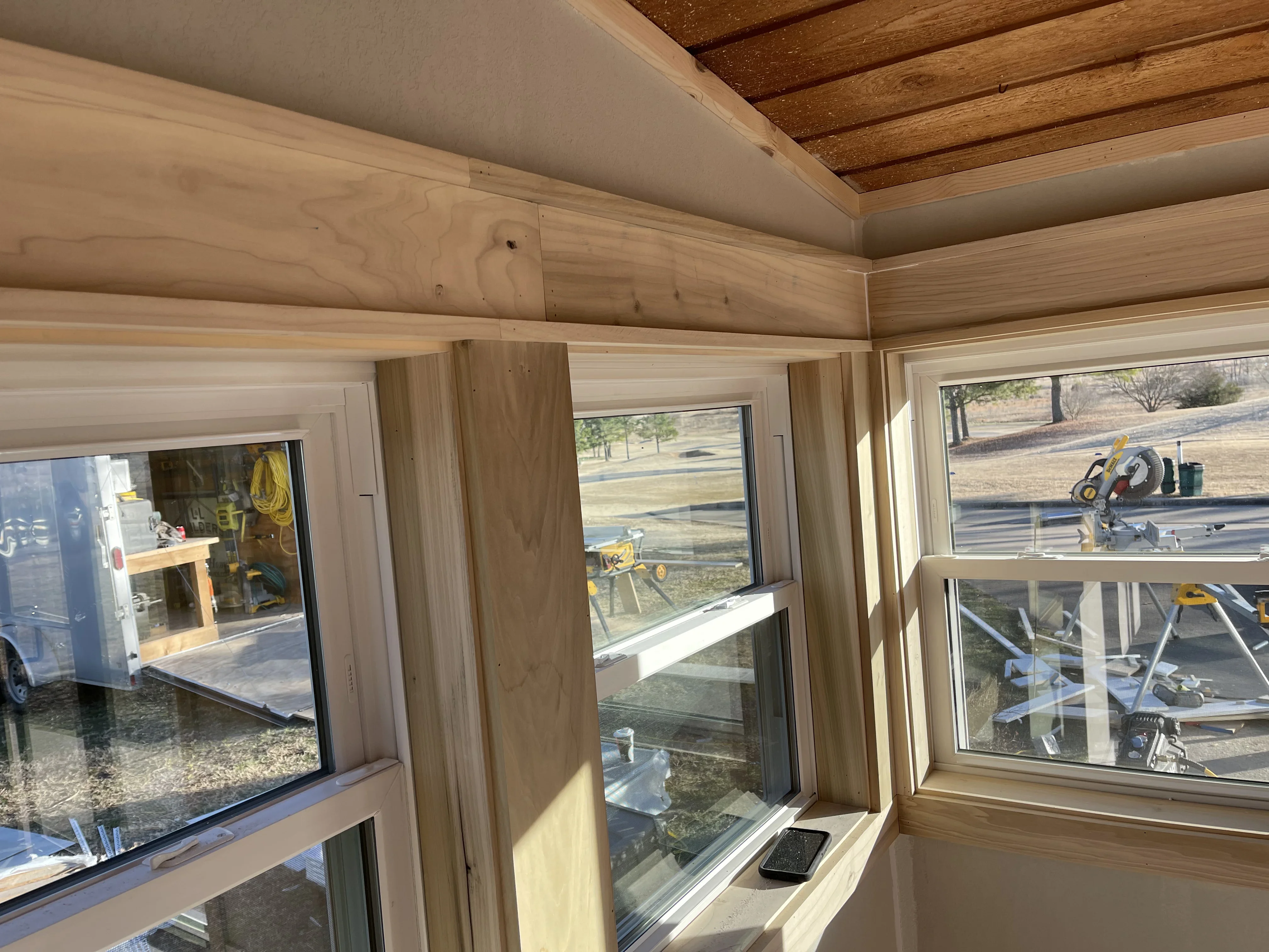 Interior room addition with exposed wood beams, drywall, and multi-pane windows with white trim
