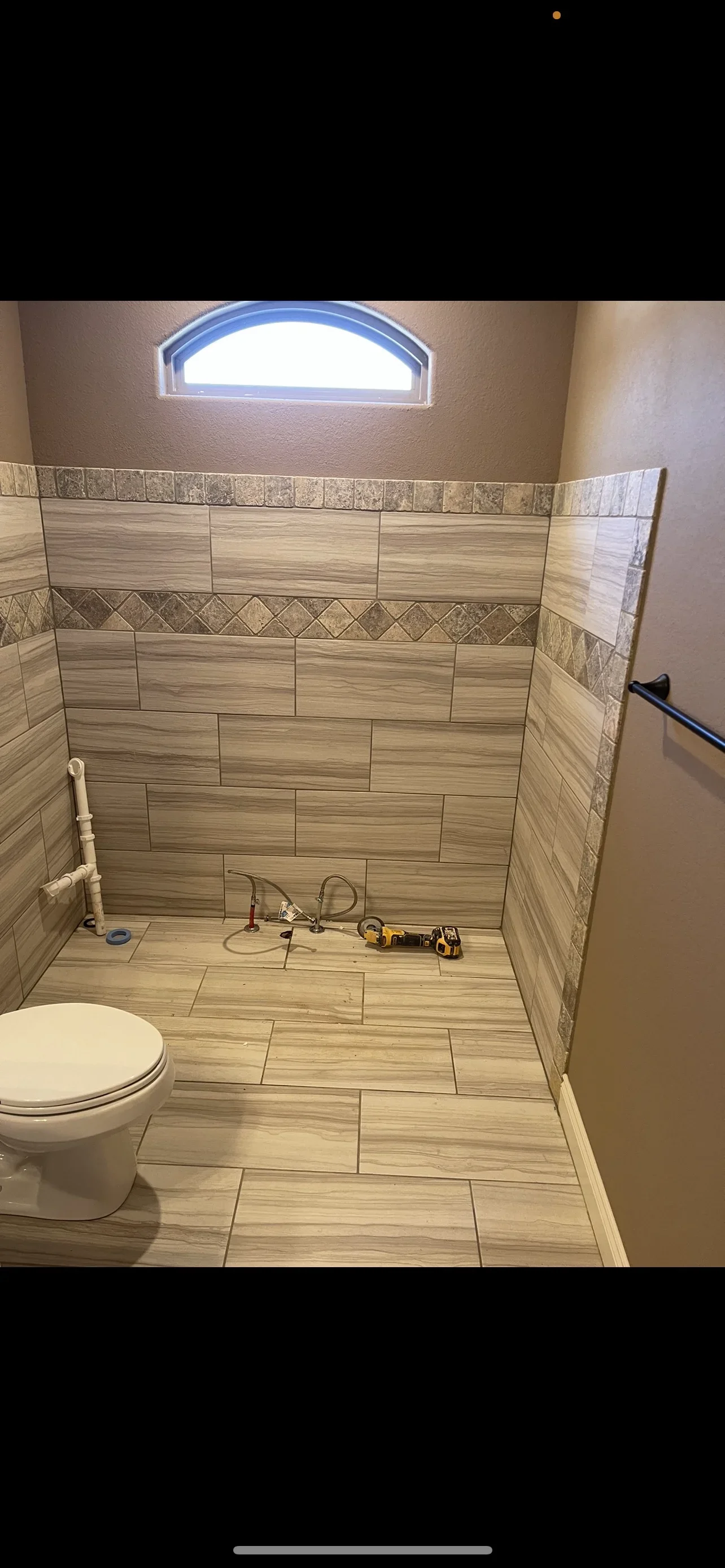 Newly tiled shower enclosure with wood-grain ceramic tile, decorative border, and arched window