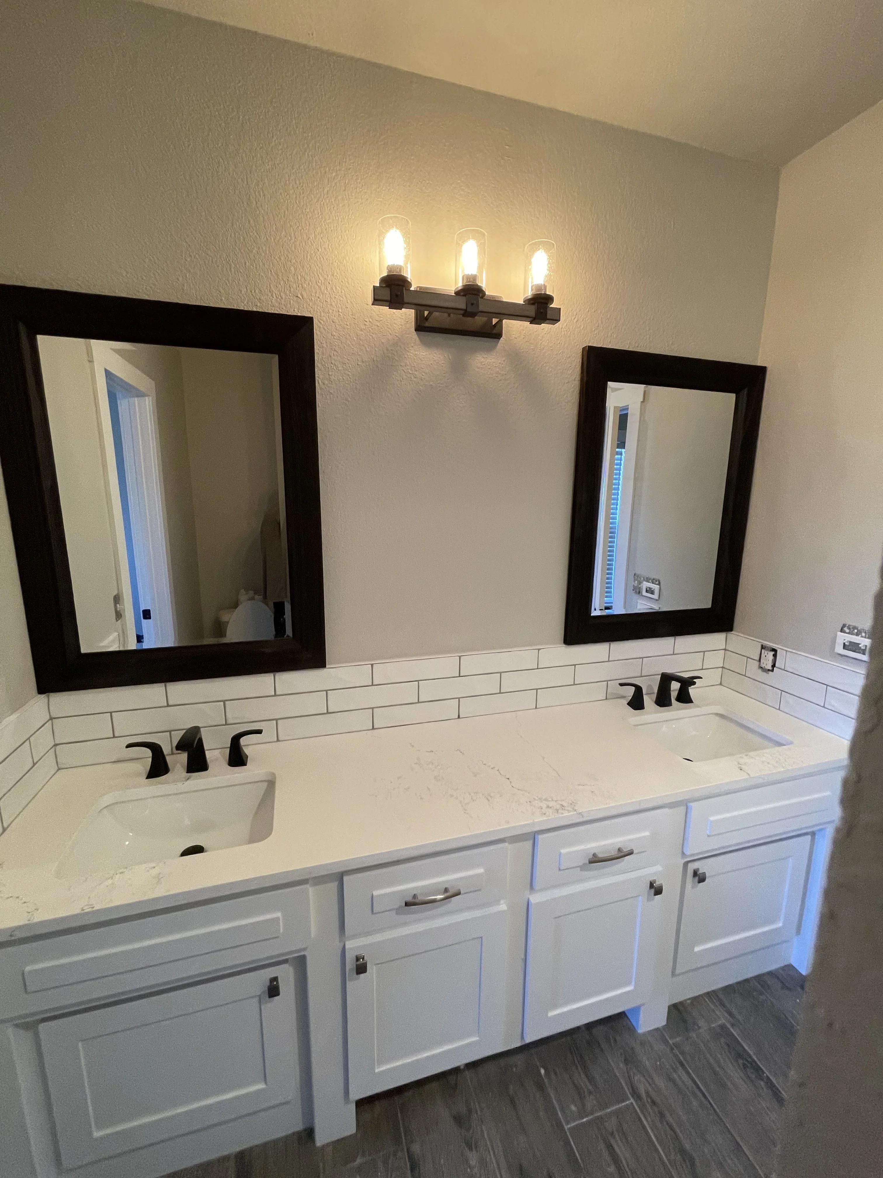 Dual-sink bathroom vanity with white cabinetry, quartz countertop, subway tile backsplash, and black-framed mirrors