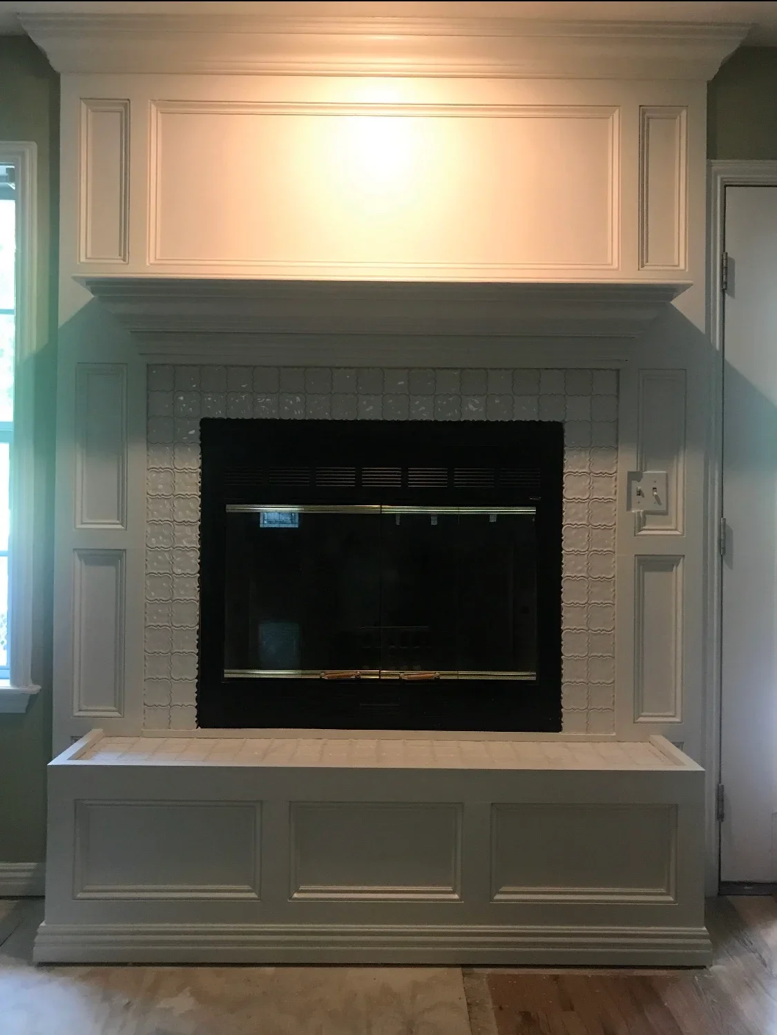 Built-in fireplace surround with raised panel cabinetry, textured tile surround, and coffered mantel with crown molding