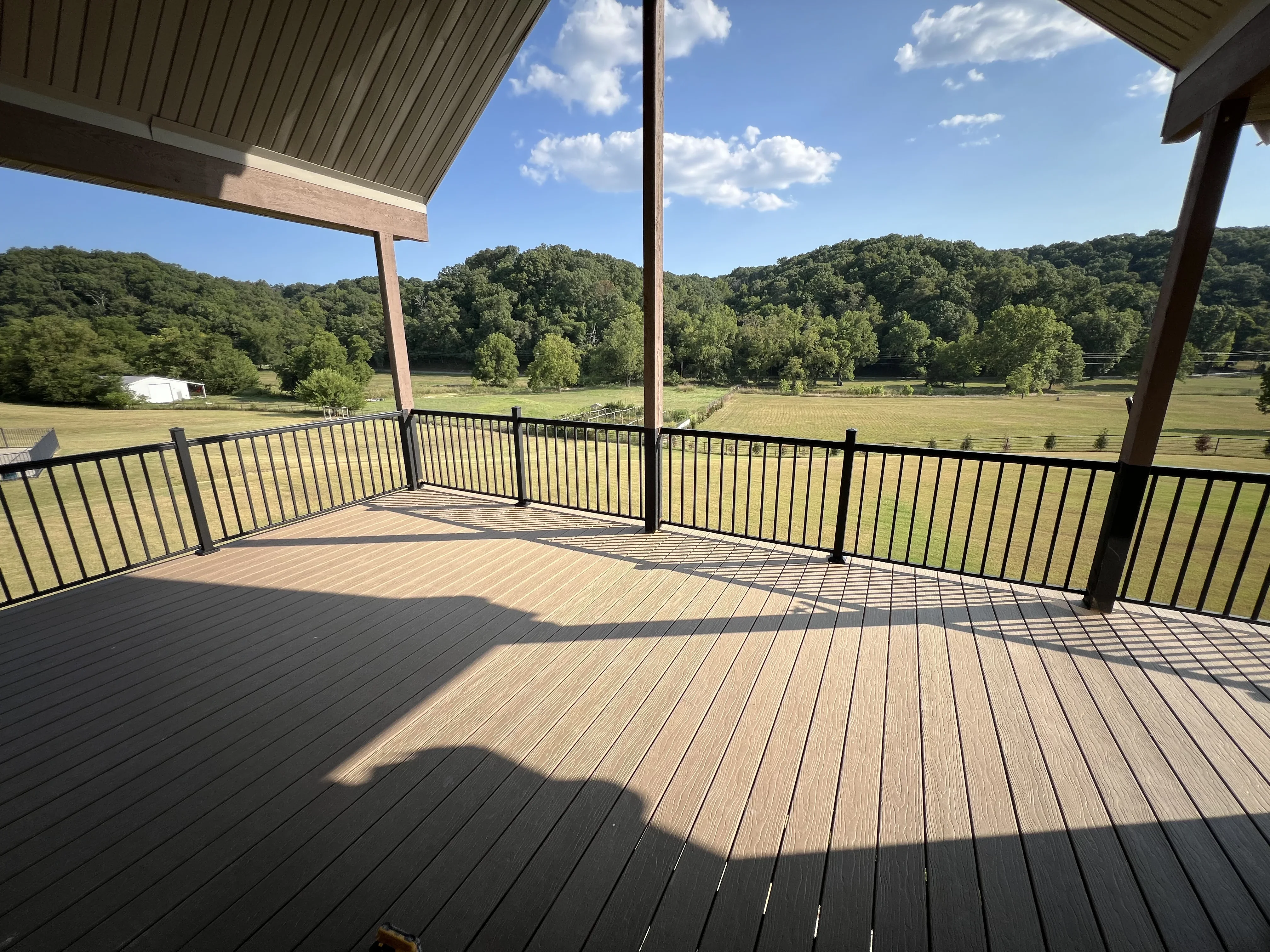 Composite deck with black metal railing and covered roof structure overlooking rural property