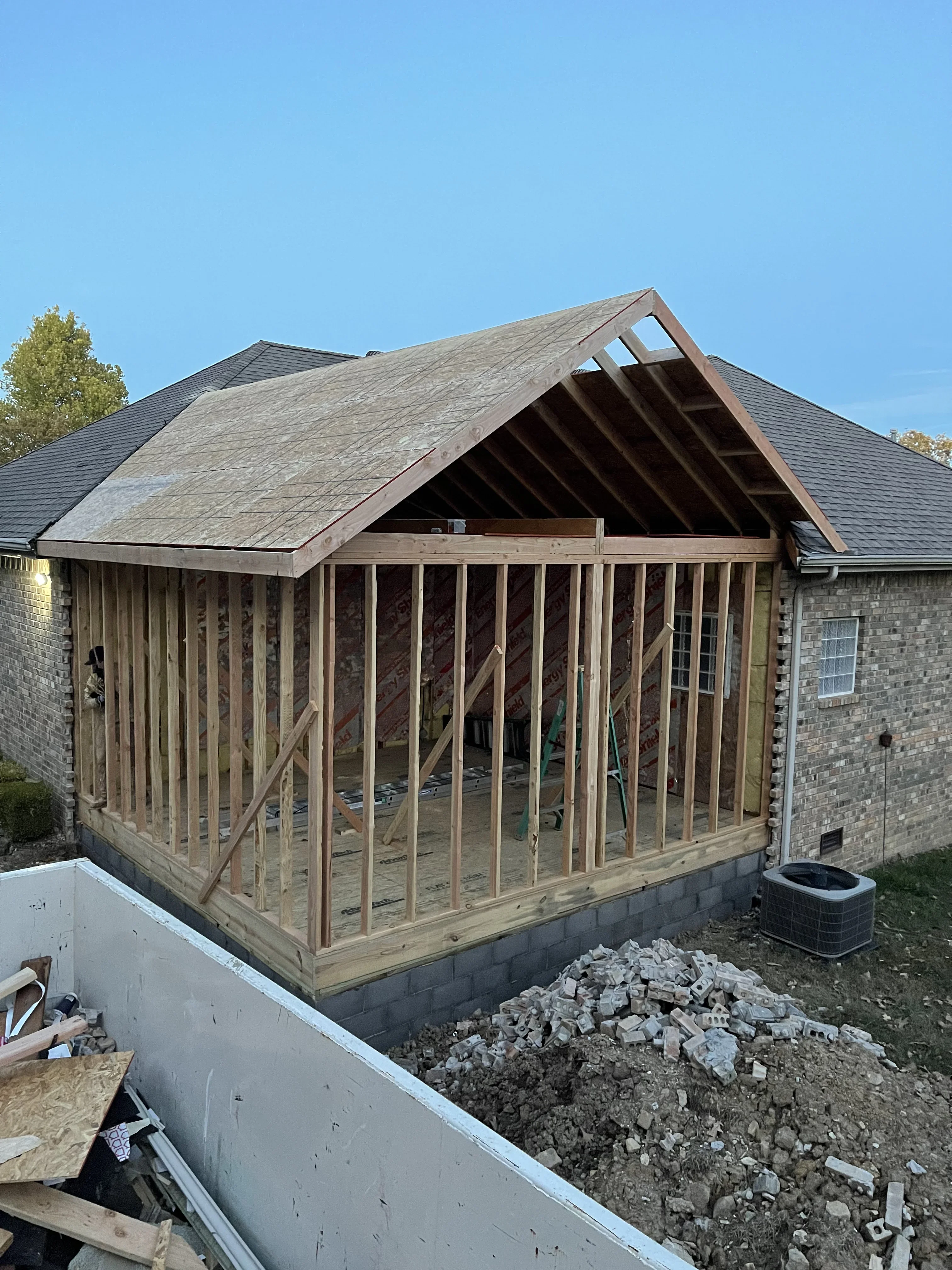 Wood-framed room addition with gable roof and large windows under construction