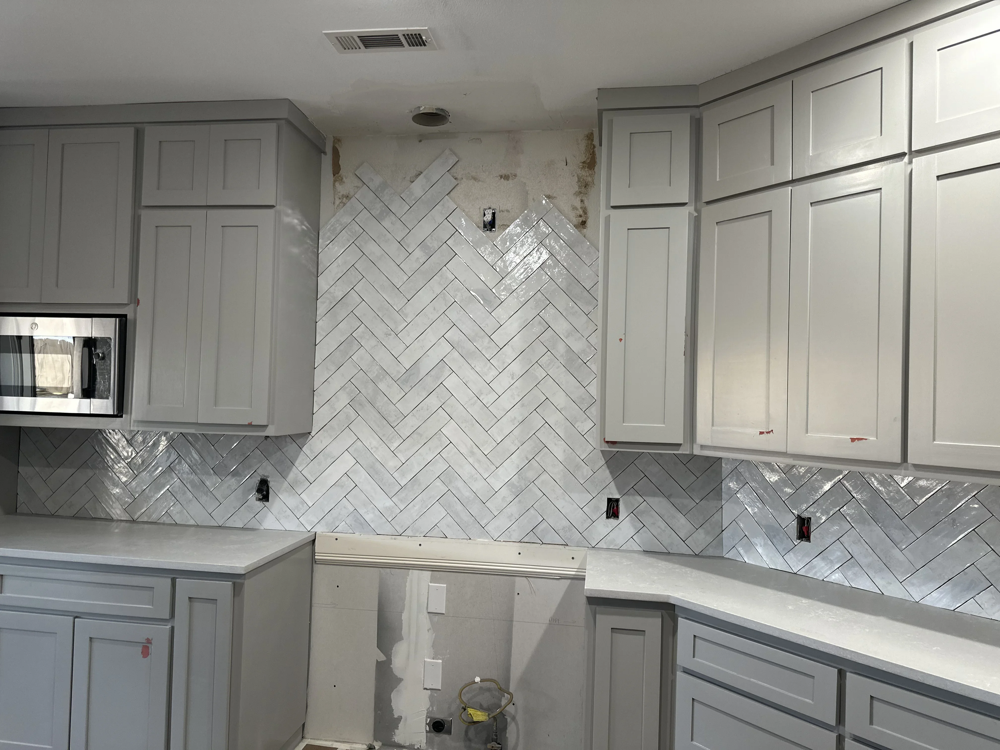 Gray kitchen cabinets with herringbone subway tile backsplash and white quartz counters